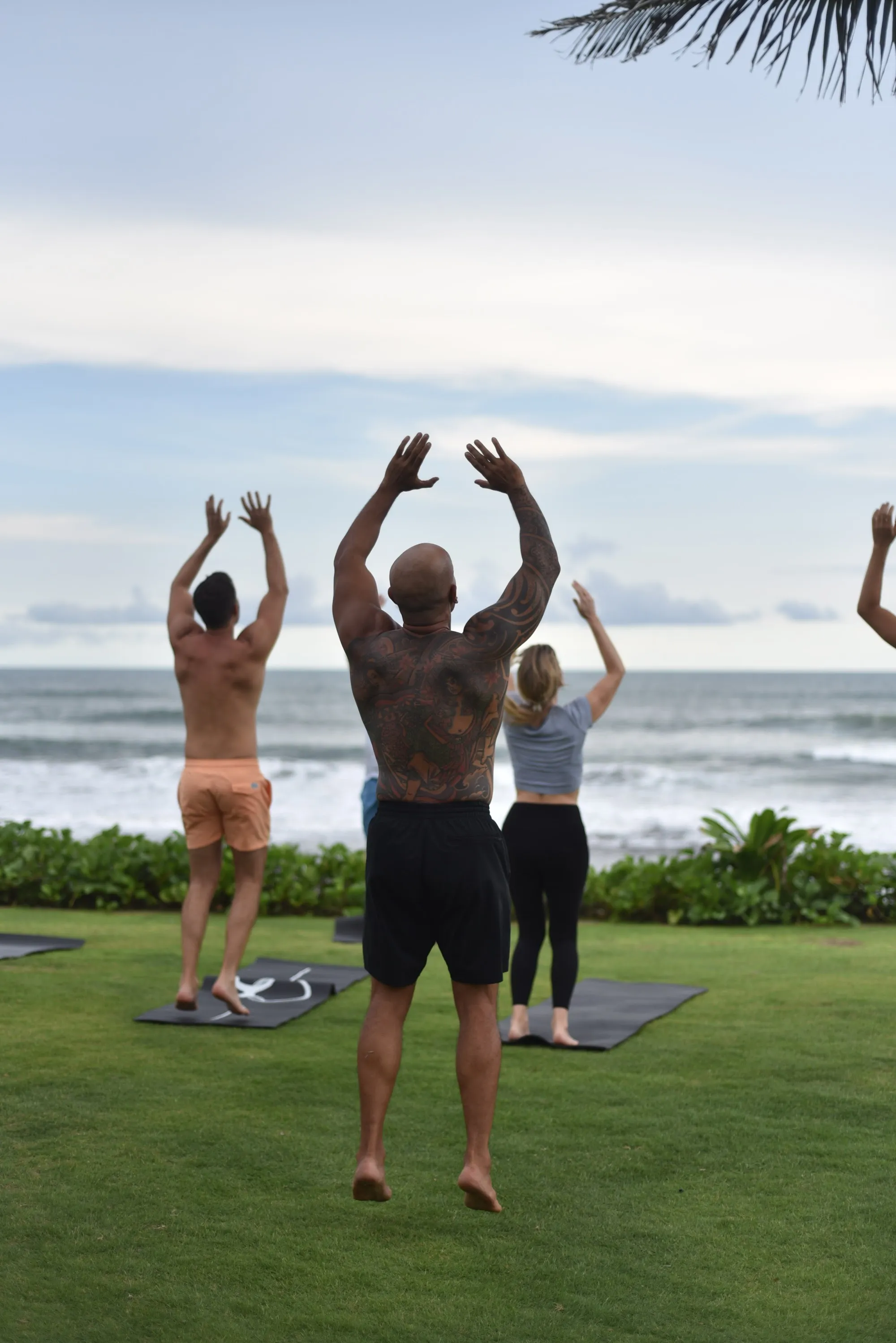 Andy leading the group in movement on the lawn by the ocean, arms raised