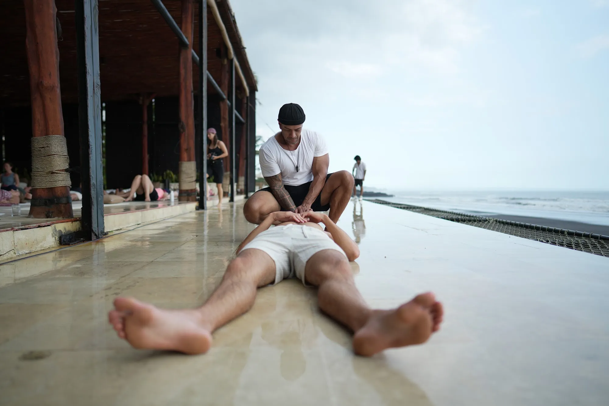 A participant resting on the floor by the ocean, Andy sitting beside him